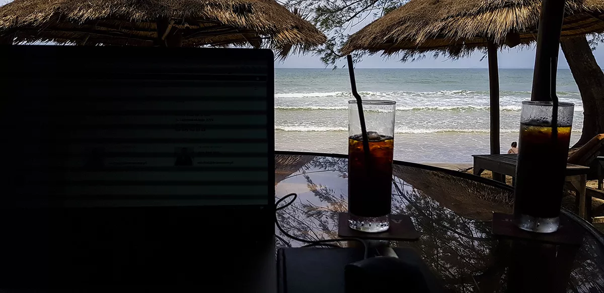 Laptop i szklanki z napojem na plaży pod palmowymi parasolami