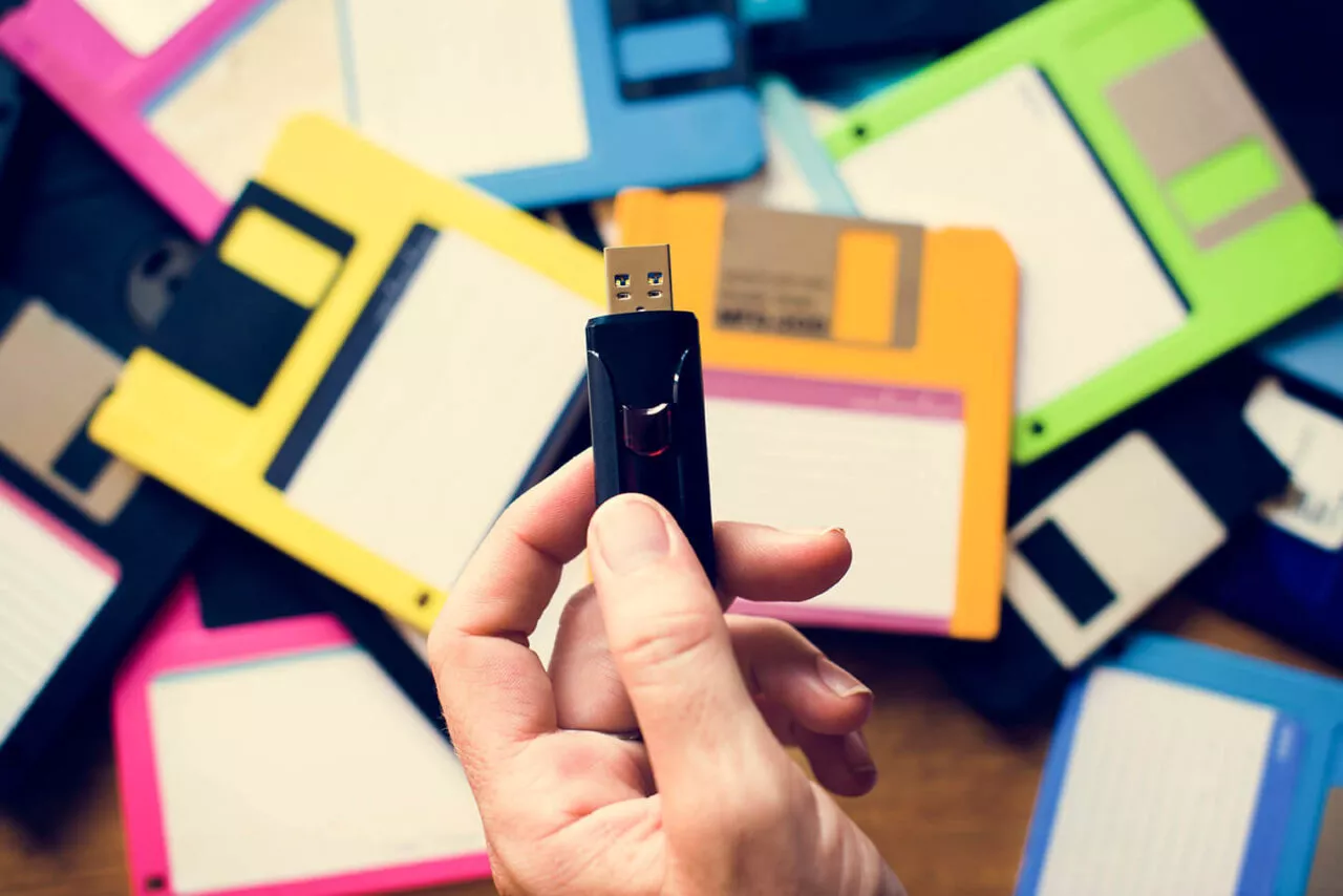 Pendrive trzymany w dłoni na tle kolorowych dyskietek